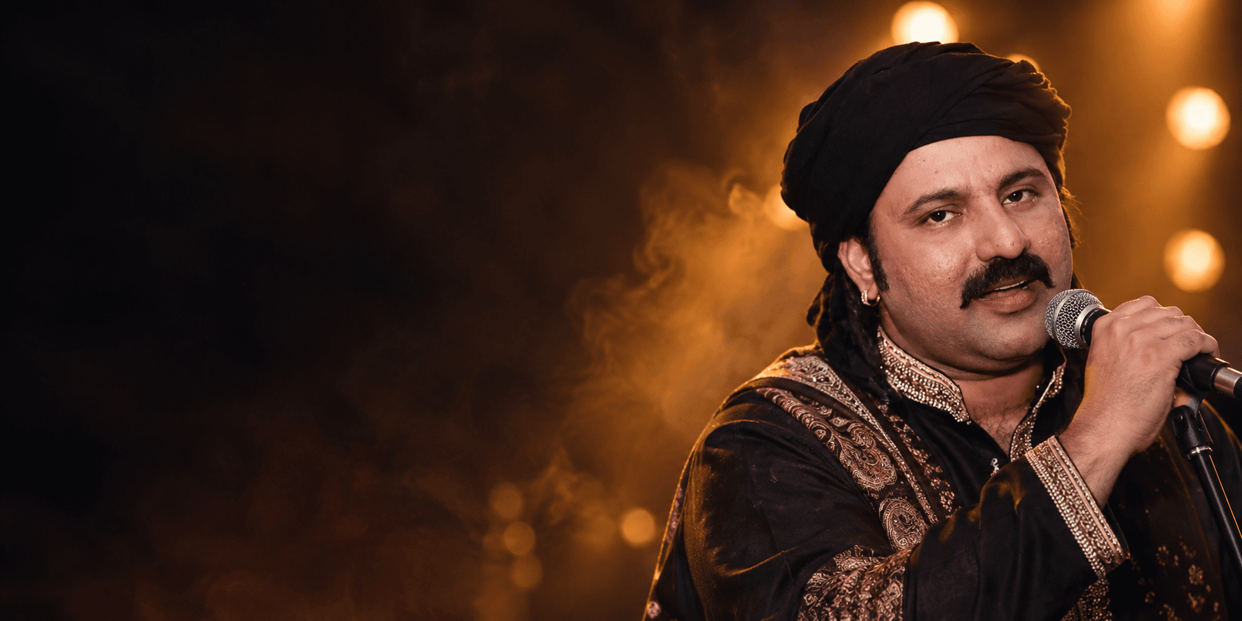 Zaheer Lohar performing with a microphone beneath warm stage lights
